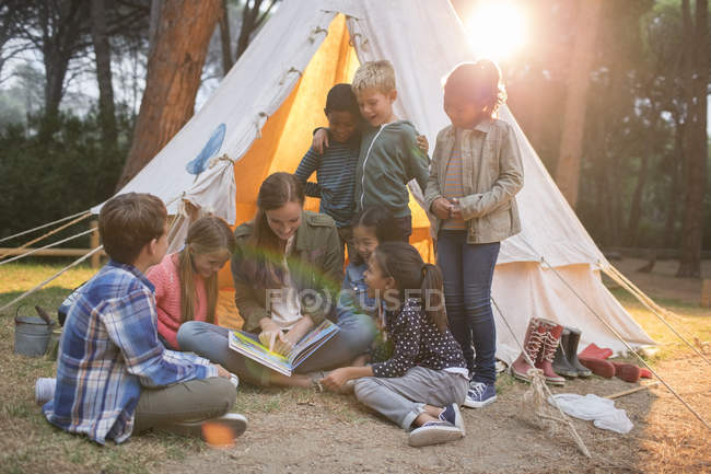 Teacher and students reading at campsite — Stock Photo