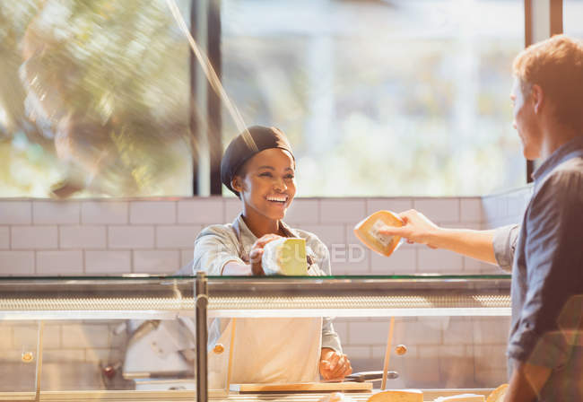 Trabalhadora sorridente servindo cliente no balcão de queijo no mercado de mercearia — Fotografia de Stock