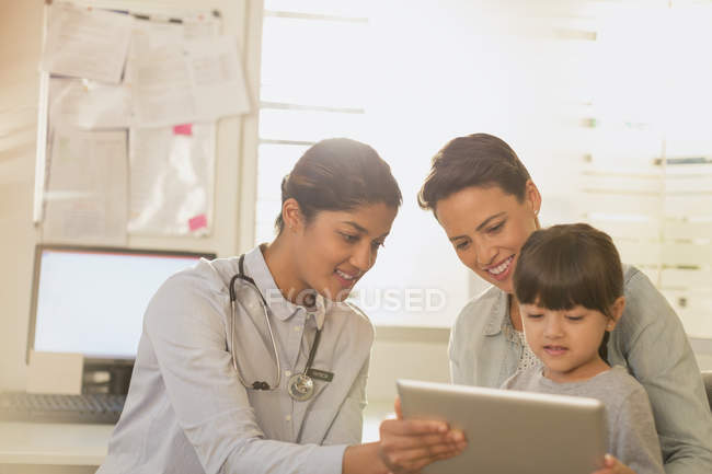 Жінка-педіатр, що показує цифровий планшет для дівчинки-пацієнта і матері в екзаменаційній кімнаті — стокове фото