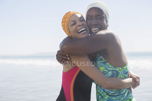 Enthusiastic women hugging in bathing suits and caps — Stock Photo