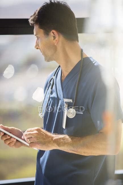 Male doctor holding tablet pc and looking out of hospital window — Stock Photo