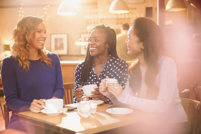 Mujeres amigas tomando café y hablando en la mesa del café - foto de stock