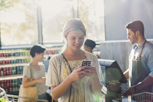 Молода жінка використовує мобільний телефон на ринку продуктових магазинів — стокове фото