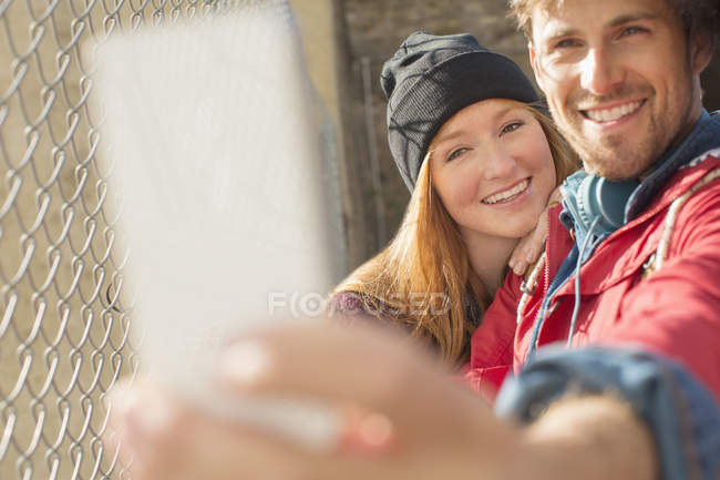 Pareja tomando autorretrato con el teléfono de la cámara al lado de la cerca del eslabón de cadena - foto de stock