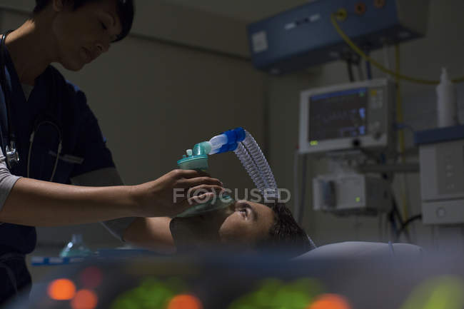 Médico sosteniendo máscara de oxígeno sobre la cara del paciente en la unidad de cuidados intensivos - foto de stock