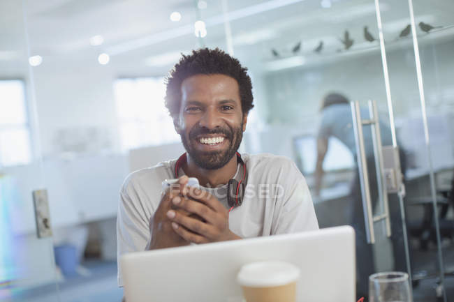 Retrato sonriente, empresario creativo seguro de usar el teléfono inteligente en el ordenador portátil en la oficina - foto de stock