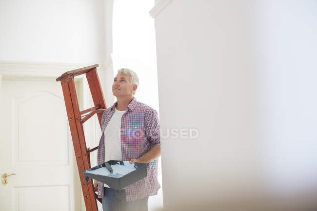 Older man carrying ladder and paint tray — Stock Photo