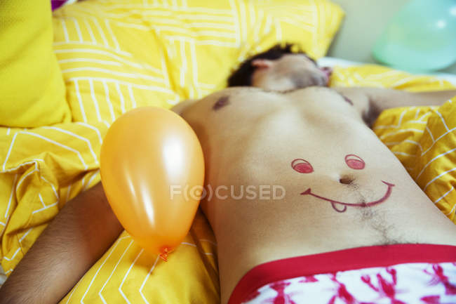 Мужчина с улыбающимся лицом, рисующий на животе, спящий после вечеринки — стоковое фото