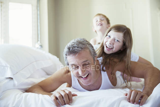 Padre e hijos jugando en la cama - foto de stock