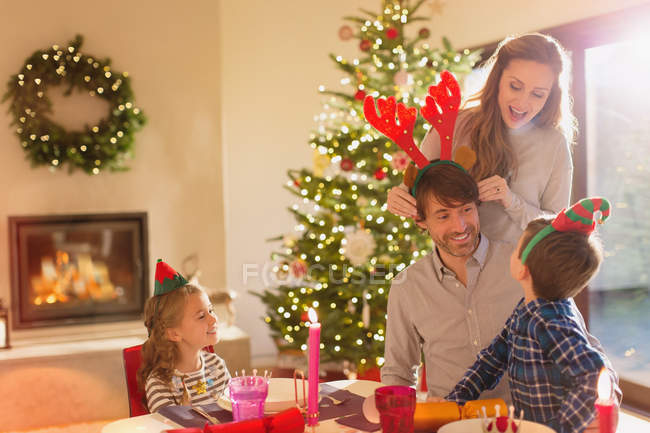 Familia vistiendo cuernos de reno elfo y traje en la mesa de comedor de Navidad - foto de stock