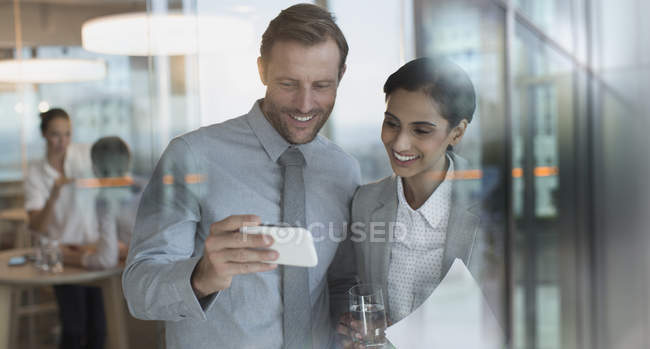 Smiling businessman and businesswoman watching video on smart phone in office — Stock Photo