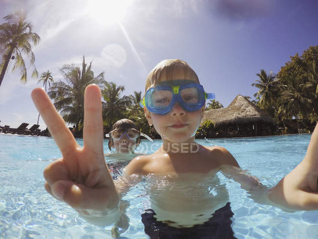 Porträt eines Jungen gestikuliert Friedenszeichen in tropischem Schwimmbad — Stockfoto