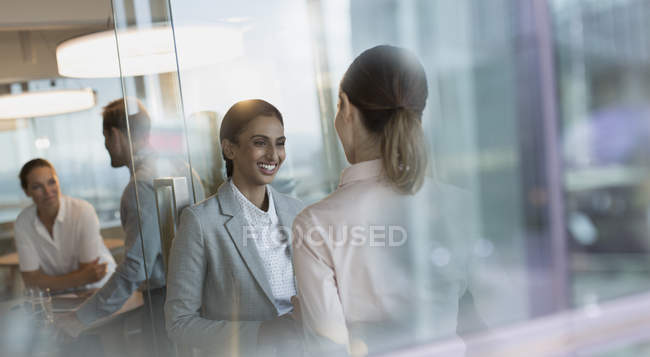 Улыбающиеся деловые женщины разговаривают в офисе — стоковое фото