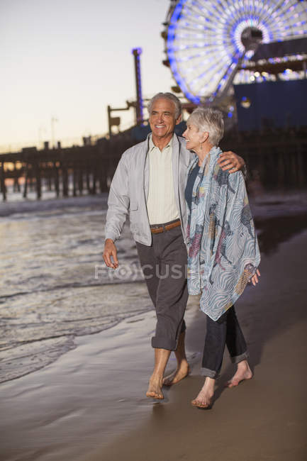 Casal sênior andando na praia ao pôr do sol — Fotografia de Stock