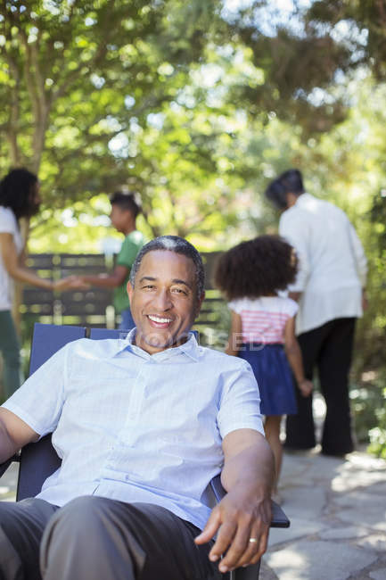 Ritratto di uomo anziano sorridente sul patio con la famiglia sullo sfondo — Foto stock