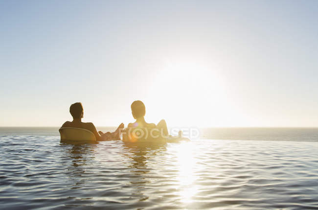 Couple in lounge chairs in infinity pool overlooking ocean — Stock Photo