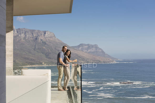 Casal olhando para a vista ensolarada do oceano a partir de varanda de luxo — Fotografia de Stock