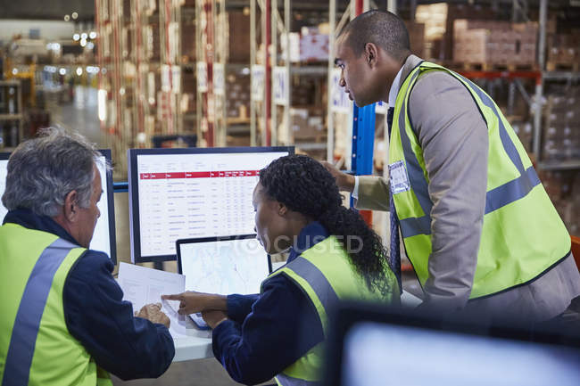 Managers meeting reviewing paperwork at laptop and computer in distribution warehouse — Stock Photo