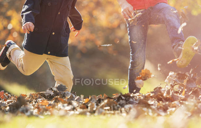 Imagen recortada de niños juguetones patadas hojas de otoño - foto de stock