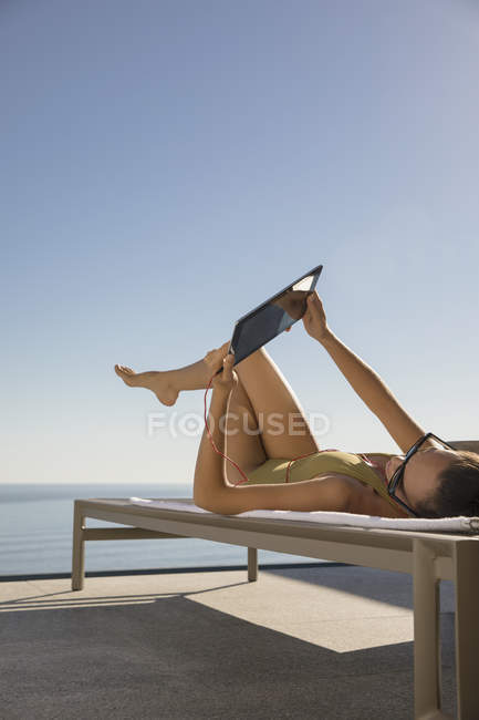 Mulher tomando banho de sol, usando tablet digital na cadeira lounge no pátio ensolarado — Fotografia de Stock