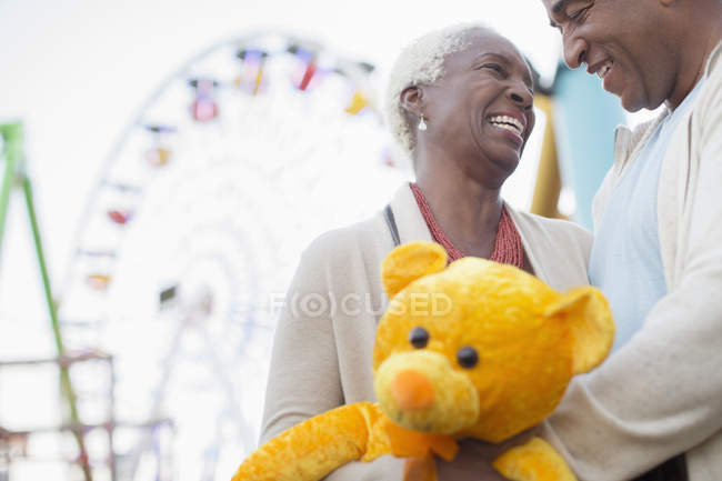 Couple aîné avec ours en peluche étreignant au parc d'attractions — Photo de stock