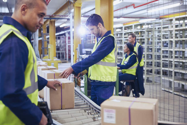 Trabajadores escaneando y procesando cajas en cinta transportadora en almacén de distribución - foto de stock
