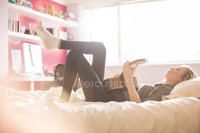 Chica adolescente tocando la guitarra en la cama - foto de stock