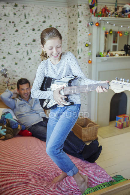 Chica tocando la guitarra para el padre en dormitorio - foto de stock
