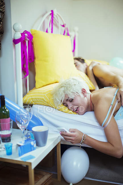 Mujer usando smartphone en la cama la mañana después de la fiesta - foto de stock
