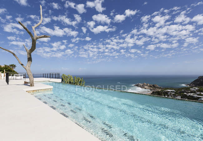 Clouds in blue sky over luxury lap pool overlooking ocean — Stock Photo