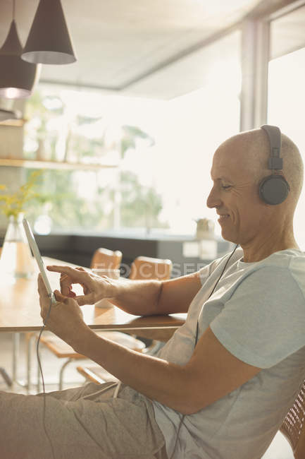 Homme mûr écoutant de la musique avec écouteurs et tablette numérique à table — Photo de stock