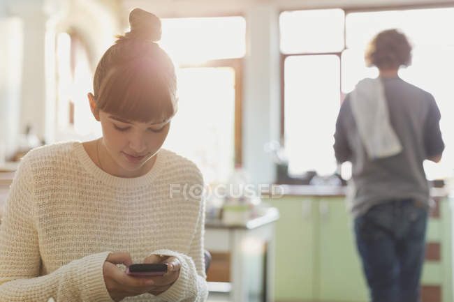 Молодая женщина смс с мобильного телефона на кухне — стоковое фото