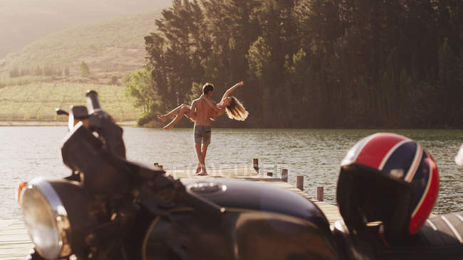 Giovane uomo che trasporta donna esuberante sul bacino lacustre dietro la moto — Foto stock