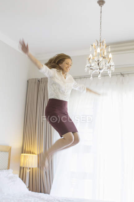 Mujer de negocios saltando en la cama en la habitación de hotel - foto de stock