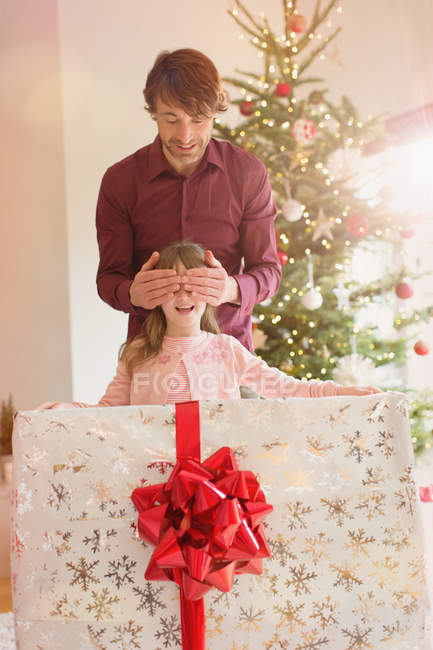 Padre cubriendo ojos de hija sosteniendo gran regalo de Navidad - foto de stock