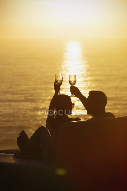 Silueta par tostadas copas de vino en el balcón con tranquilo atardecer vista al mar - foto de stock