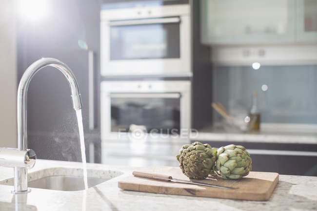 Alcachofras em tábua de corte na cozinha doméstica moderna — Fotografia de Stock