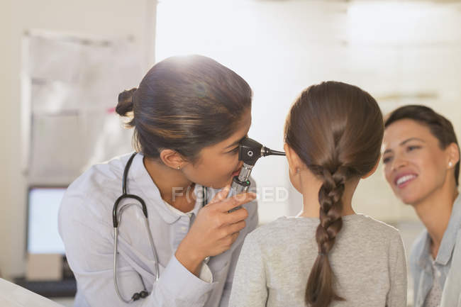 Female pediatrician using otoscope, checking ear of girl patient in examination room — Stock Photo