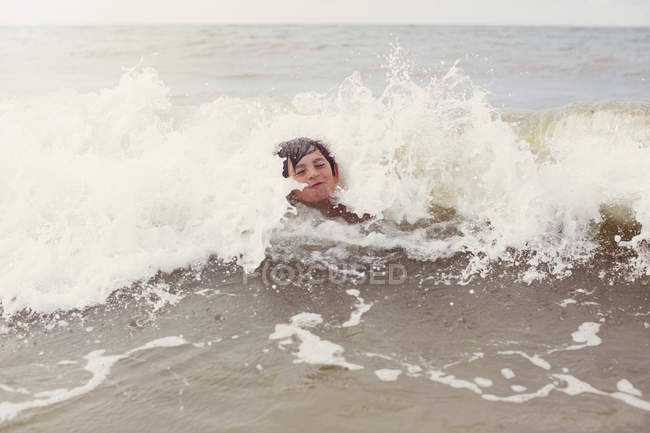 Waves splashing around boy swimming in summer ocean — Stock Photo