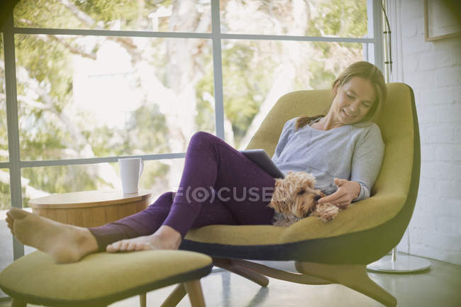 Frau mit Laptop entspannt und Streichelhund auf Stuhl — Stockfoto