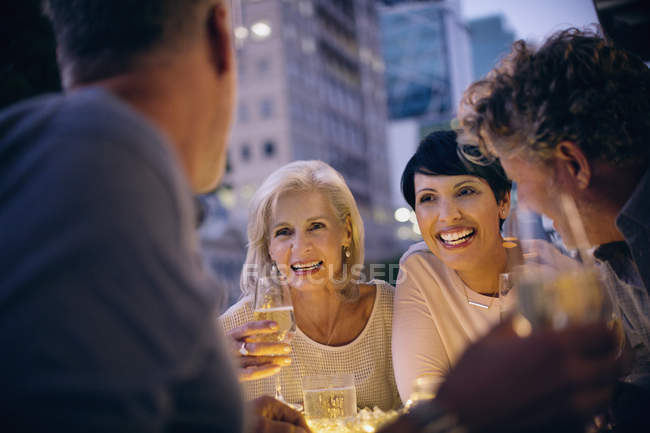Couples souriants buvant du vin blanc et parlant au café de trottoir urbain — Photo de stock