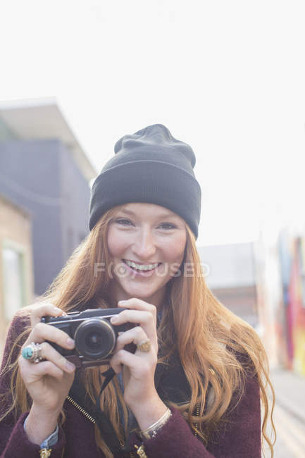 Happy young woman using camera on city street — Stock Photo