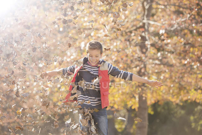 Niño juguetón jugando en hojas de otoño - foto de stock