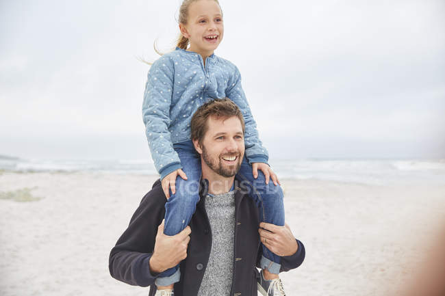 Батько, що носить дочку на плечах на зимовому пляжі — стокове фото