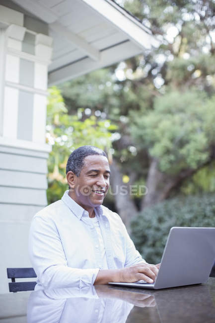 Пенсионер с ноутбуком за столиком во дворе — стоковое фото