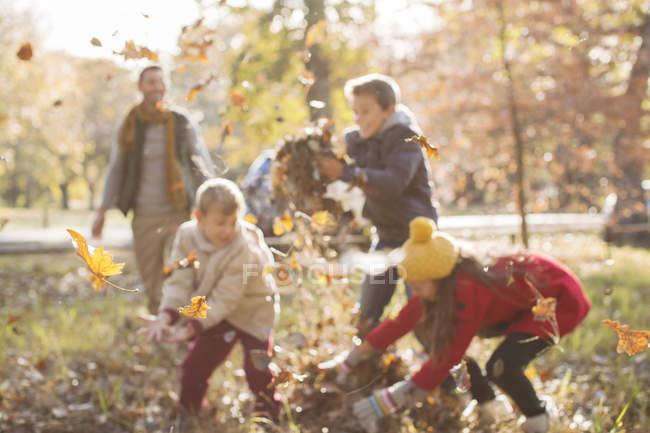 Семья играет в осенние листья в парке — стоковое фото