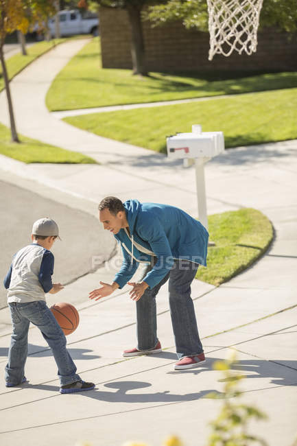 Padre e hijo jugando baloncesto en la soleada entrada - foto de stock