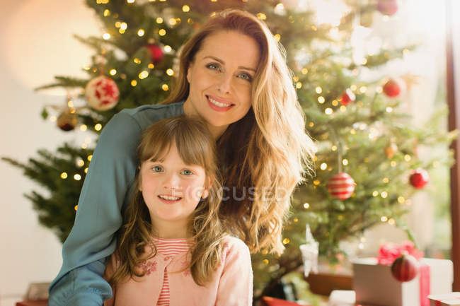 Retrato sorridente mãe e filha na frente da árvore de Natal — Fotografia de Stock
