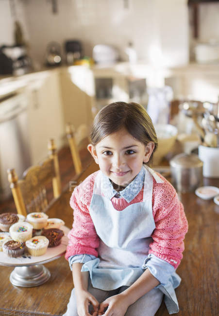 Giovane ragazza seduta sul tavolo della cucina vicino cupcakes — Foto stock