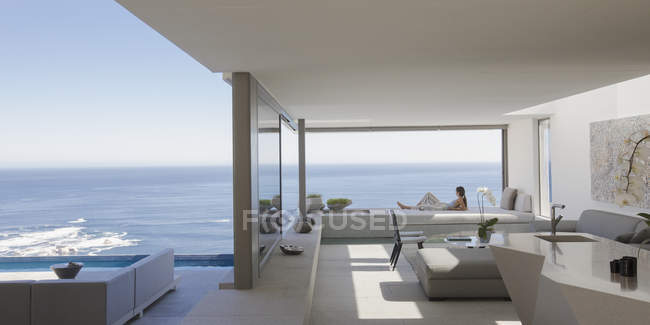 Жінка розслабляється на сучасному, розкішному будинку вітрина патіо з сонячним видом на океан — стокове фото
